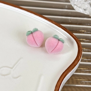 Macro shot of sweet pink flocked peach earrings with green leaf detail on a ceramic plate