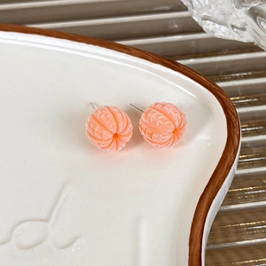 Close-up of orange flocked fruit earrings with knitted texture on ceramic tray