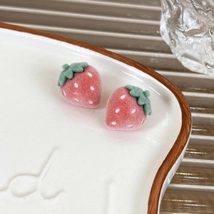 Close-up of pink flocked strawberry stud earrings with green leaves on ceramic tray