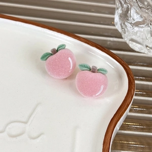 Close-up of pink flocked peach stud earrings with green leaves on a white ceramic plate