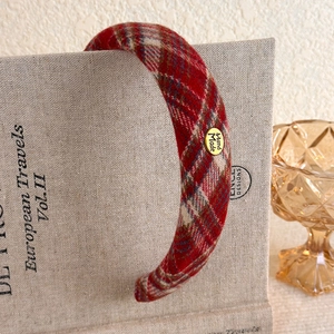 Detailed view of a red plaid headband with 'Hand Made' golden charm on a vintage book
