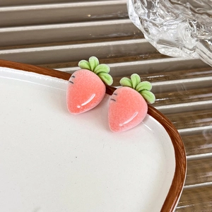 Detailed close-up of pink flocked strawberry earrings with green leaf on a ceramic plate