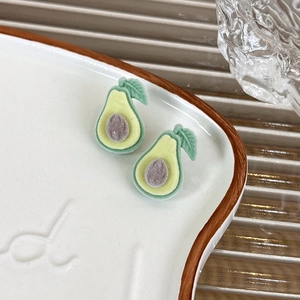 Macro detail of avocado stud earrings with fuzzy flocked texture on a white plate