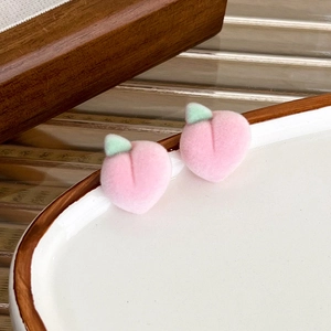 Close-up of pink flocked peach stud earrings with green leaf detail on a ceramic dish