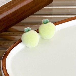 Detailed close-up of cute green flocked apple stud earrings on white ceramic plate
