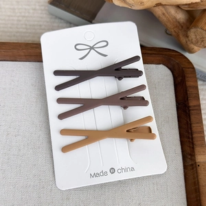 Detailed view of three matte brown cross-shaped hair clips on white card packaging