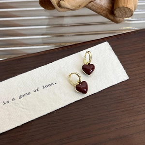 Detail of red enamel heart earrings with gold metal hoops on a white textured background