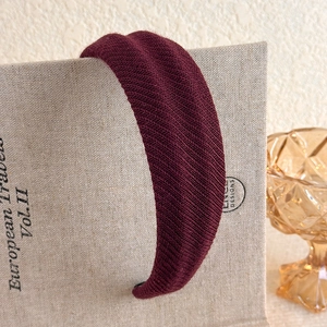 Close-up of wine red ribbed knit headband with thick texture on linen book