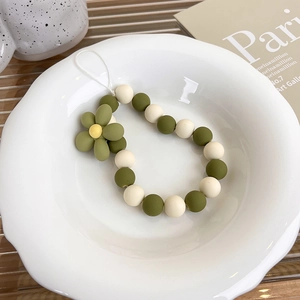 Detail of beaded phone strap with olive green flowers and matte pearls in a ceramic dish
