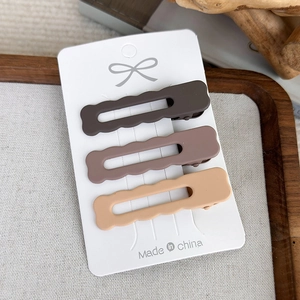 Detailed view of three matte brown wavy hair clips on a white card display