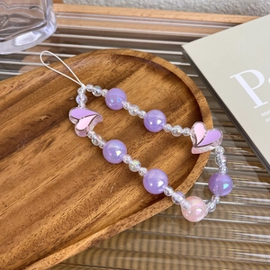 Macro detail of purple aurora beaded phone strap with heart charms on wooden tray