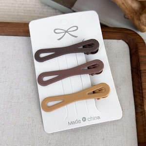 Three-piece set of matte brown hair clips in earthy tones on a rustic wooden tray