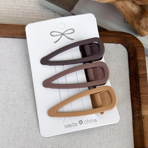 Macro detail of three matte brown seamless hair clips on a white display card pack