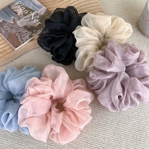 Detail view of five soft organza scrunchies in pastel colors on a textured background