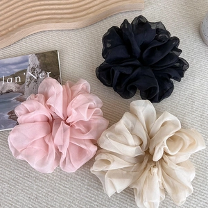 Three large organza scrunchies in black, pink, and ivory on a natural wood surface