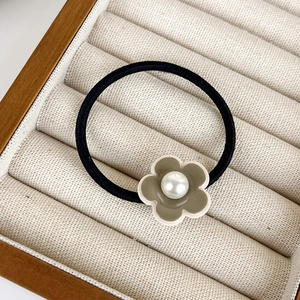 Détail d'un élastique à cheveux fleur verte avec perle centrale sur tissu beige