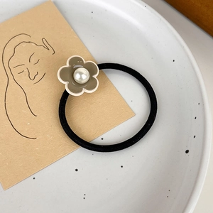 Détail d'un élastique à cheveux avec perle blanche et pétales marron sur un plat en céramique
