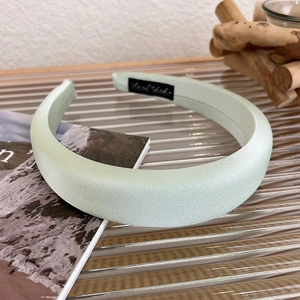 Detail view of a pale green satin sponge headband with a black Hand Made woven label
