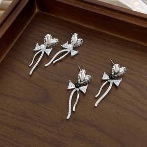 Macro detail of silver heart bow earrings with pearls and zircon on dark wood