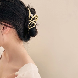 Détail de la pince à cheveux dorée ondulée avec perle sur une coiffure élégante