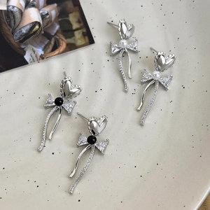 Sweet bow and heart pearl earrings with long diamond-encrusted ribbons on ceramic dish