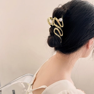 Détail d'une grande pince à cheveux dorée avec perle portée sur un chignon élégant