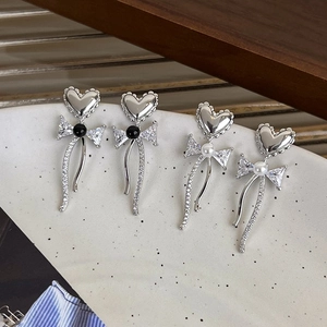 Detail view of silver bow drop earrings with heart studs and elegant pearls on a wooden tray