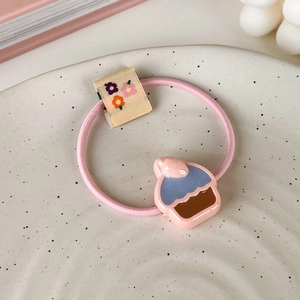 Gros plan d'un élastique rose avec breloque cupcake en résine et étiquette brodée de fleurs