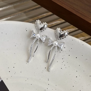 Close-up of heart bow pearl earrings with zircon inlay on a ceramic jewelry tray