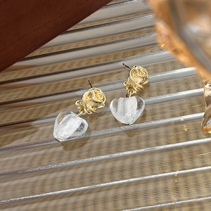 Close-up of golden rose stud earrings with translucent heart-shaped glass pendants