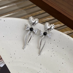Detail of silver bow heart earrings with zircon tassels on a ceramic surface