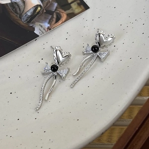 Detail of asymmetrical heart bow earrings with pearls and zircon on ceramic tray