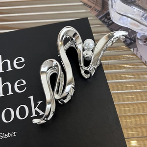 Détail d'une pince à cheveux argentée ondulée avec une perle blanche sur un livre