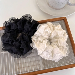 Detail of black and beige sheer mesh scrunchies on a glass tray with a ceramic cup