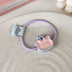 Détail d'un élastique à cheveux violet avec un ours rose et une étiquette Happy