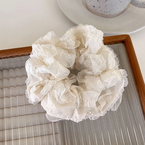Detail of elegant cream mesh scrunchie with layered ruffles on a glass tray