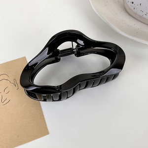 Détail d'une pince à cheveux noire brillante au design ondulé sur une surface blanche