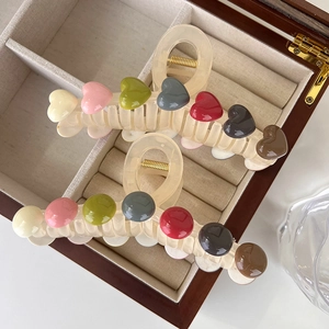 Large cream-colored hair claw clips with colorful heart and round patterns on wood