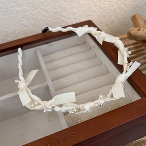 Détail d'un serre-tête en tissu crème avec perles et nœuds posé sur une boîte en bois