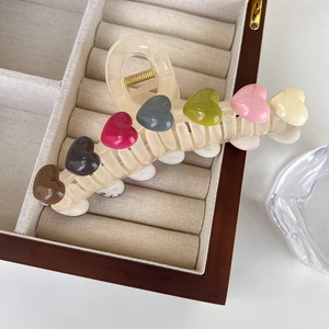 Detail of a large beige hair claw clip with colorful 3D heart shapes on velvet display