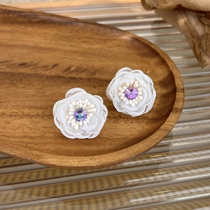 Detailed close-up of white mesh flower earrings with purple crystal centers on wooden tray