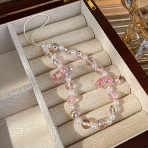 Detail of pink crystal and pearl cloud phone charm on a wooden jewelry display