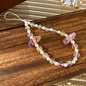Macro detail of iridescent beads, white pearls and pink resin bear charms on phone strap