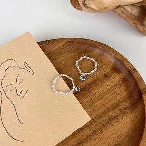 Artistic 45-degree view of silver beaded rings with blue crystal pendants on wood