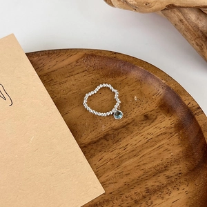 Close-up of silver beaded ring with a blue crystal pendant on a rustic wooden tray
