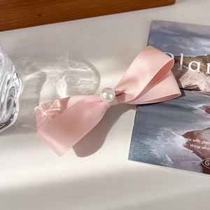 Detail einer hellrosa Satin-Schleifen-Haarklammer mit Perle in sanfter Beleuchtung