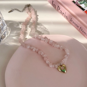 Gros plan du collier en pierres roses avec un pendentif cœur doré à motif fleuri