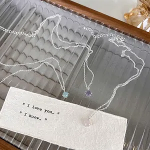 Trois colliers minimalistes en argent avec pendentifs en cristal sur plateau en bois
