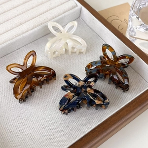 Detail of four hollow butterfly hair claws in acetate colors on a light wooden tray