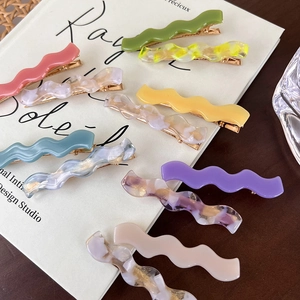Close-up of wavy acetate hair clips with marble patterns and golden metal base clips